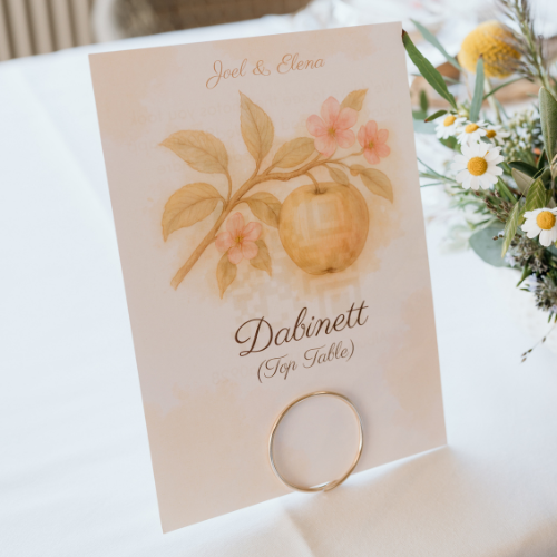 A table name card featuring an illustration of an apple tree branch. The reverse side includes a QR code that guests can scan to share photos from the wedding.