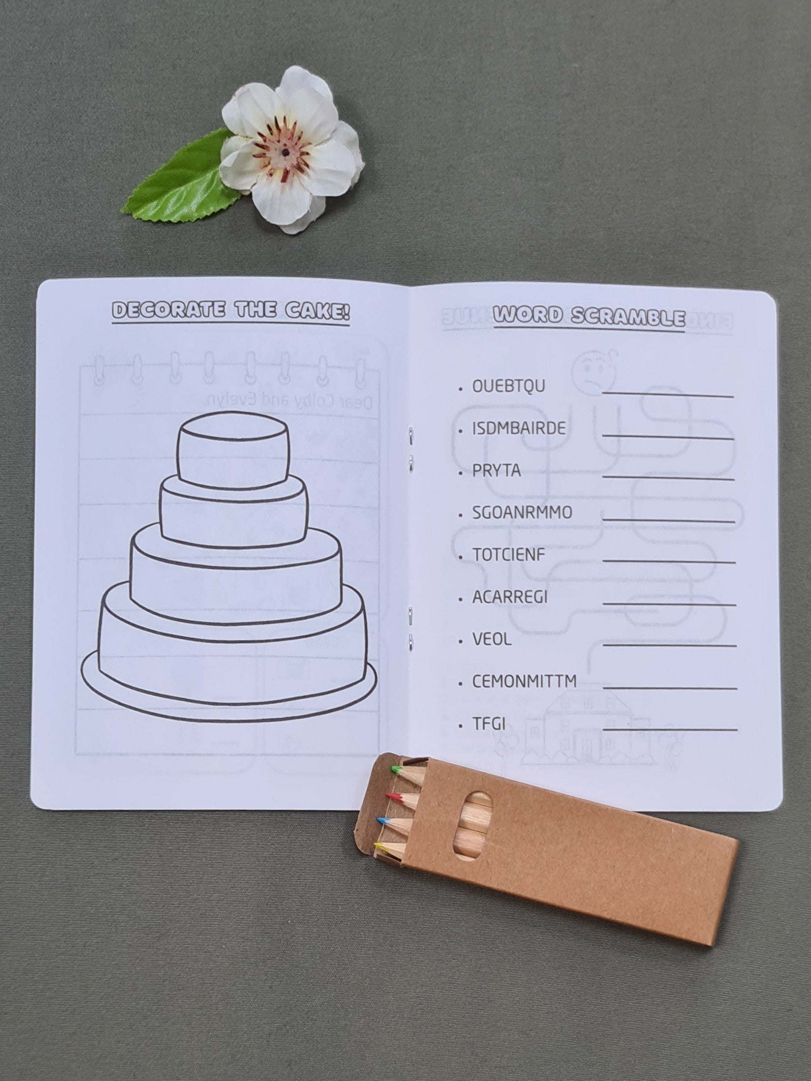 Inside pages of a personalised wedding activity booklet for kids, showing the 'Decorate the Cake' and 'Word Scramble' activities. Coloured pencils included.
