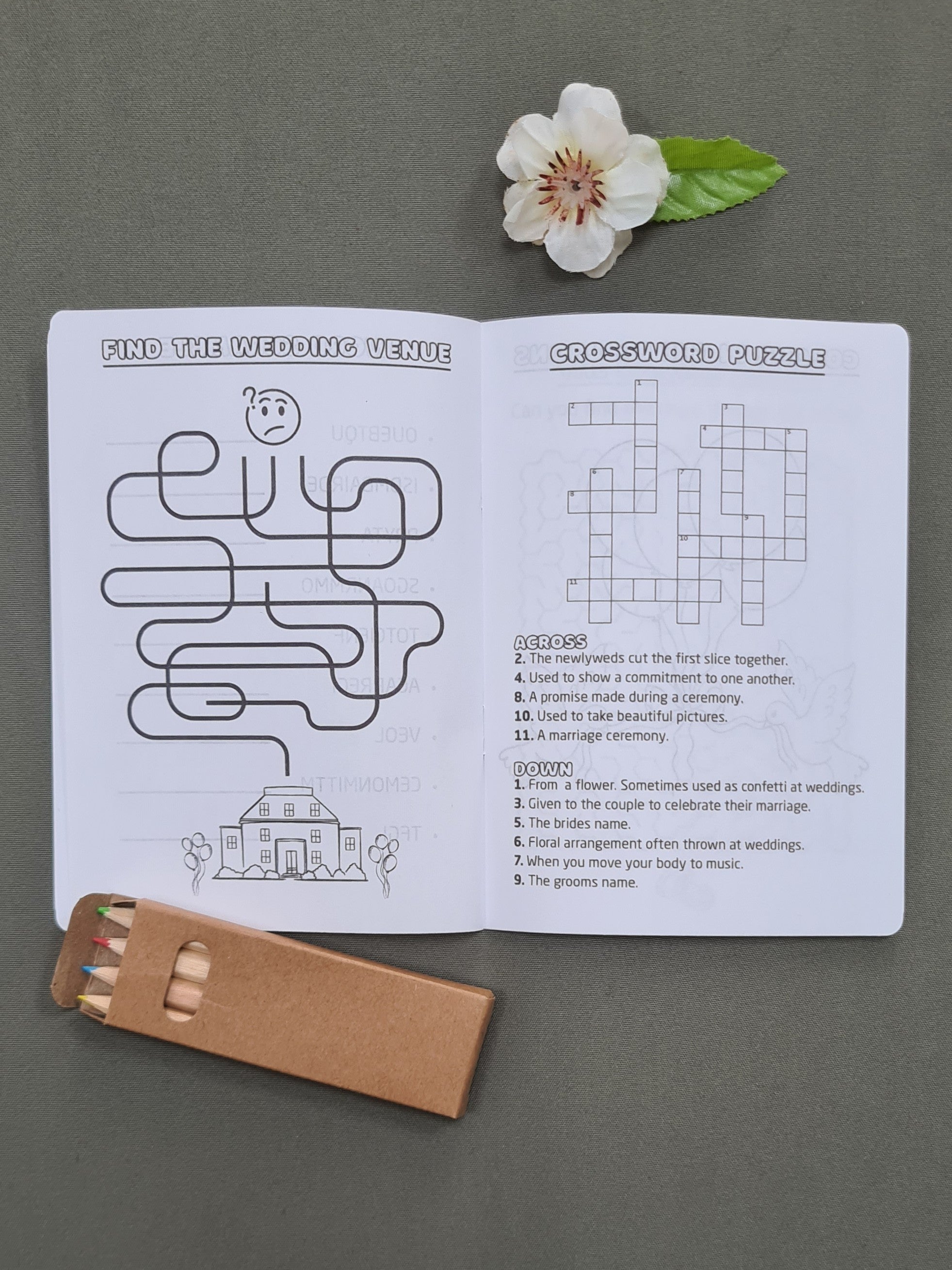 Inside pages of a personalised wedding activity booklet for kids, showing the 'Find the Wedding Venue' and 'Crossword Puzzle' activities. Coloured pencils included.